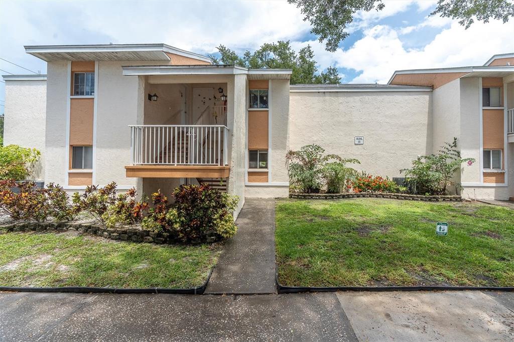 A two-story stucco apartment building features a raised entryway, a balcony, and landscaped front yards — 675 99TH AVENUE N UNIT 102, ST PETERSBURG, FL