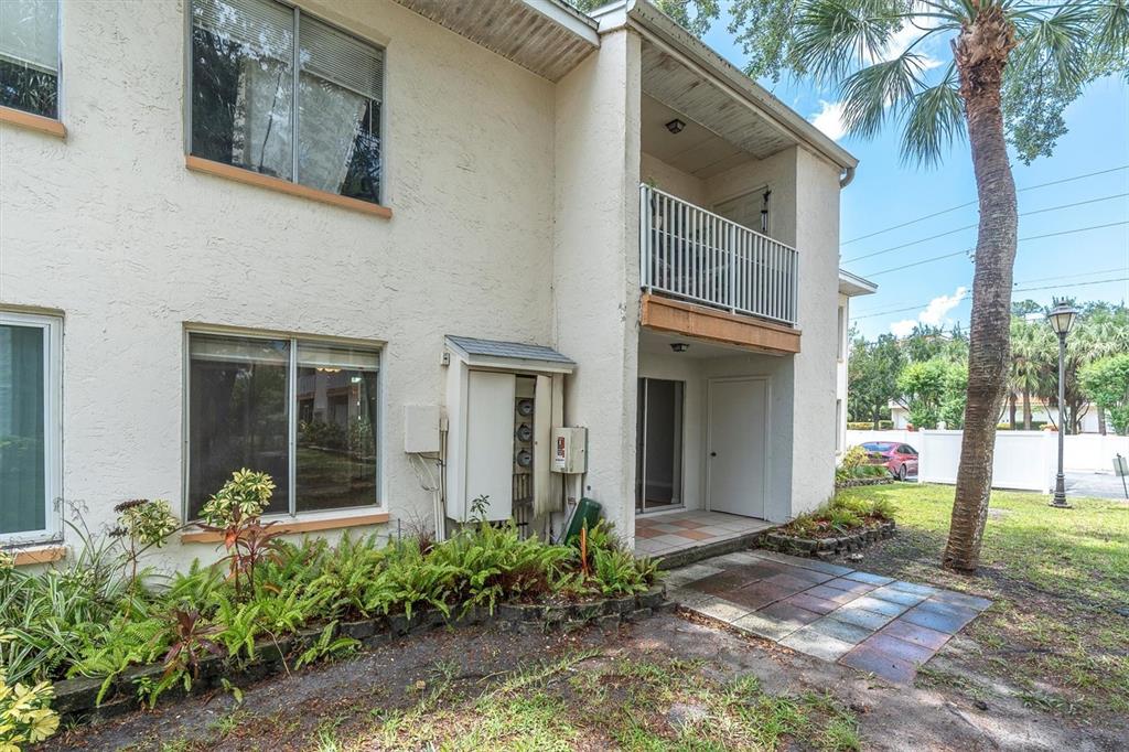The exterior of a two-story apartment building features a balcony, patio, and landscaped garden — 675 99TH AVENUE N UNIT 102, ST PETERSBURG, FL