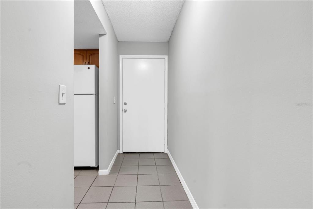 A hallway with gray walls, tiled flooring, and a white door leading to a kitchen — 675 99TH AVENUE N UNIT 102, ST PETERSBURG, FL