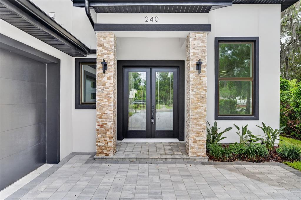 A modern home exterior features a stone-clad entryway, double glass doors, and a paved driveway — 240 N PHELPS AVENUE, WINTER PARK, FL