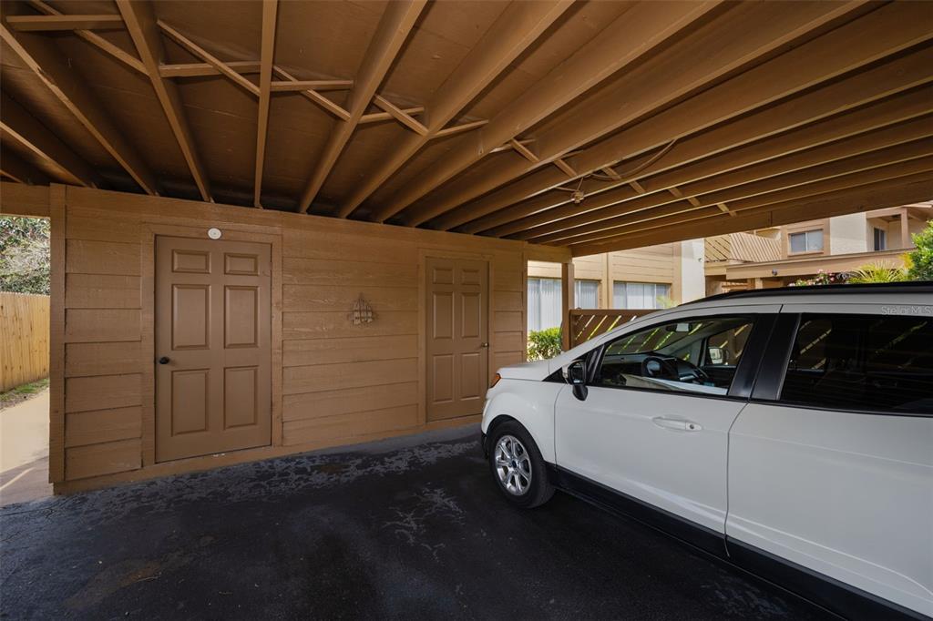 A white car is parked under a wooden carport next to two storage closet doors — 3815 PENRICK DRIVE UNIT 0, NEW PORT RICHEY, FL