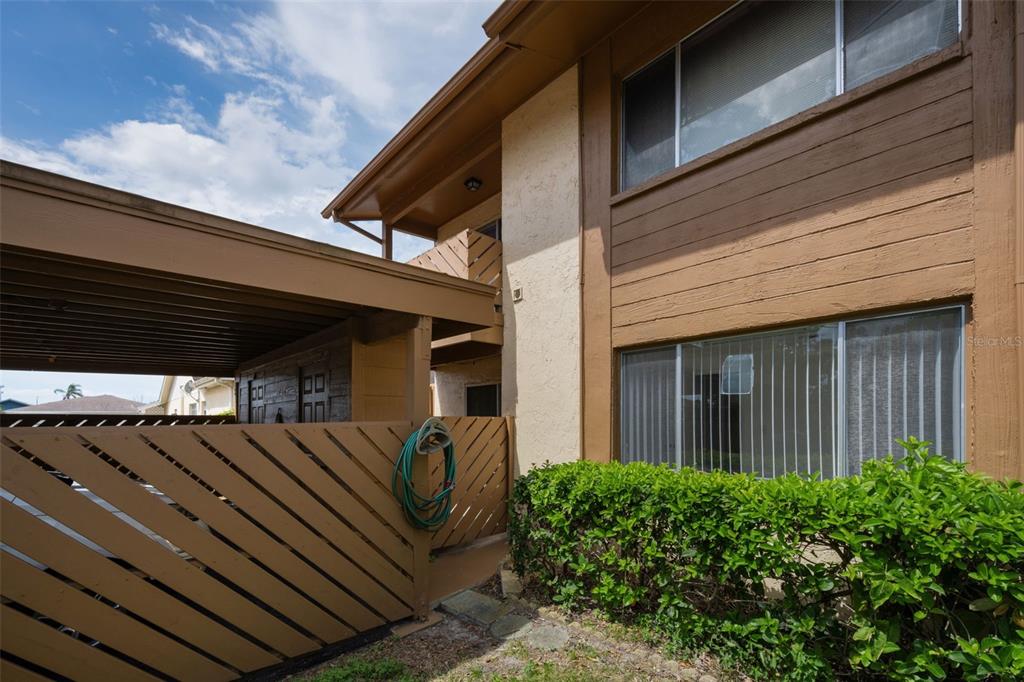 A two-story building exterior features a brown wooden carport, a slatted privacy fence, and landscaping — 3815 PENRICK DRIVE UNIT 0, NEW PORT RICHEY, FL
