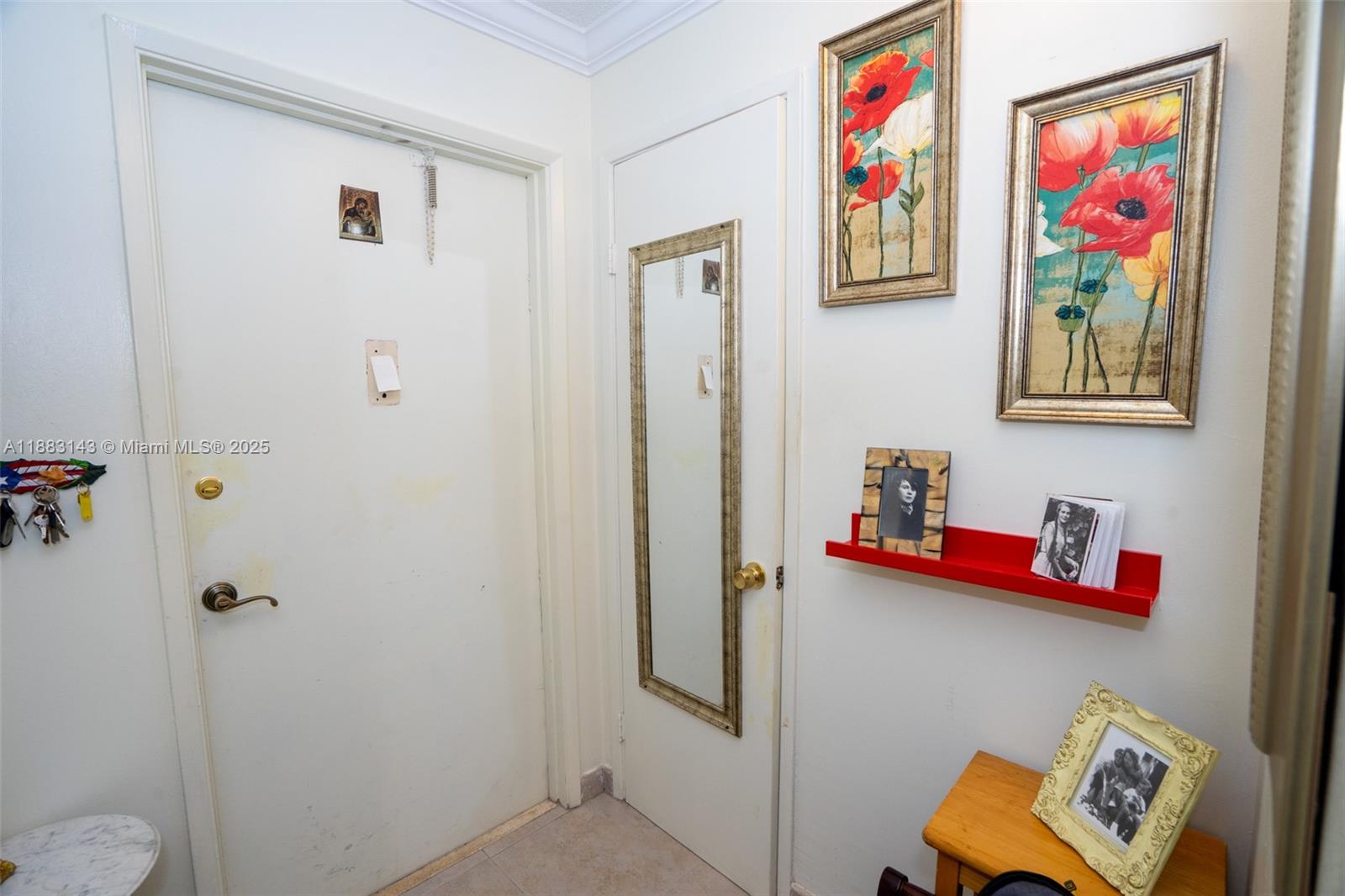 An entryway features two white doors, framed floral artwork, and a red wall-mounted shelf — 1000 NE 14th Ave # 207, Hallandale Beach FL 33009, HALLANDALE BEACH, FL