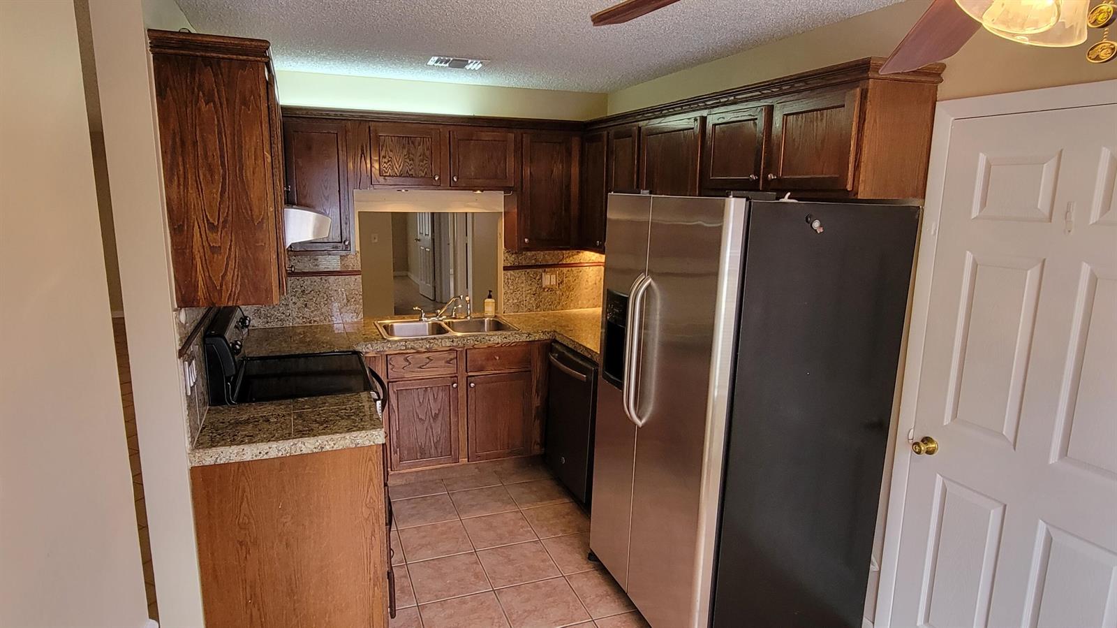 A kitchen features dark wood cabinets, granite countertops, tile flooring, and stainless steel appliances — 10056 Boynton Place Circle, Boynton Beach FL 33437, BOYNTON BEACH, FL
