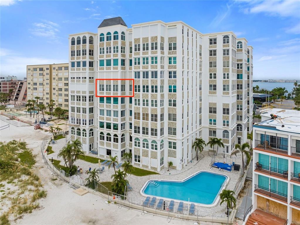 An exterior view of a multi-story white condominium building with a pool and beach access — 4950 GULF BOULEVARD UNIT 605, ST PETE BEACH, FL