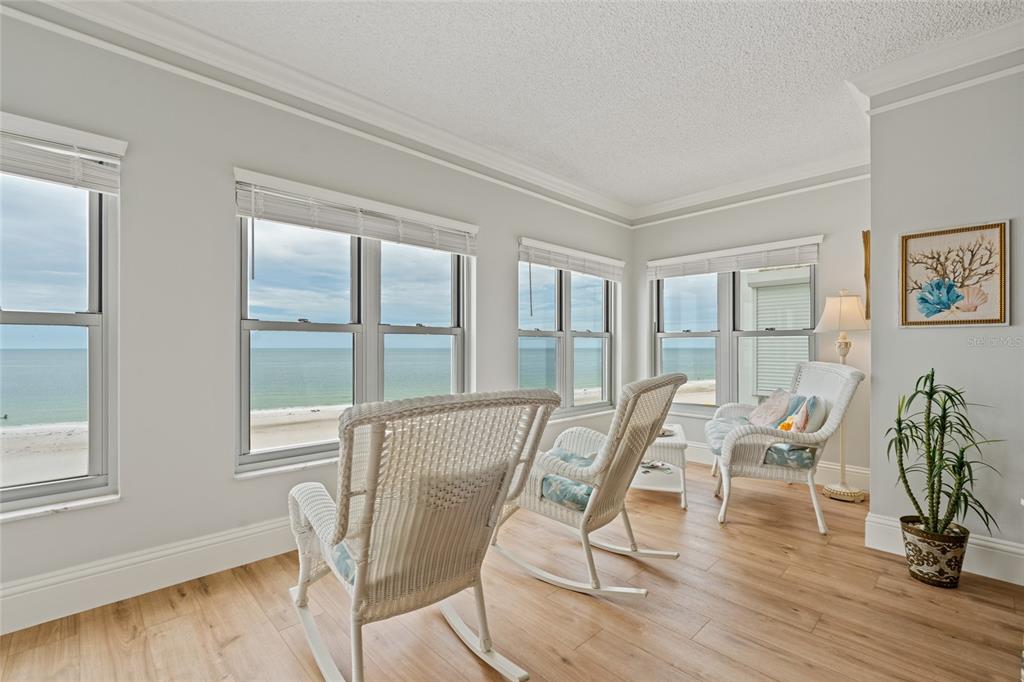 A sunroom with white wicker chairs, light wood flooring, and large windows overlooking the ocean — 4950 GULF BOULEVARD UNIT 605, ST PETE BEACH, FL