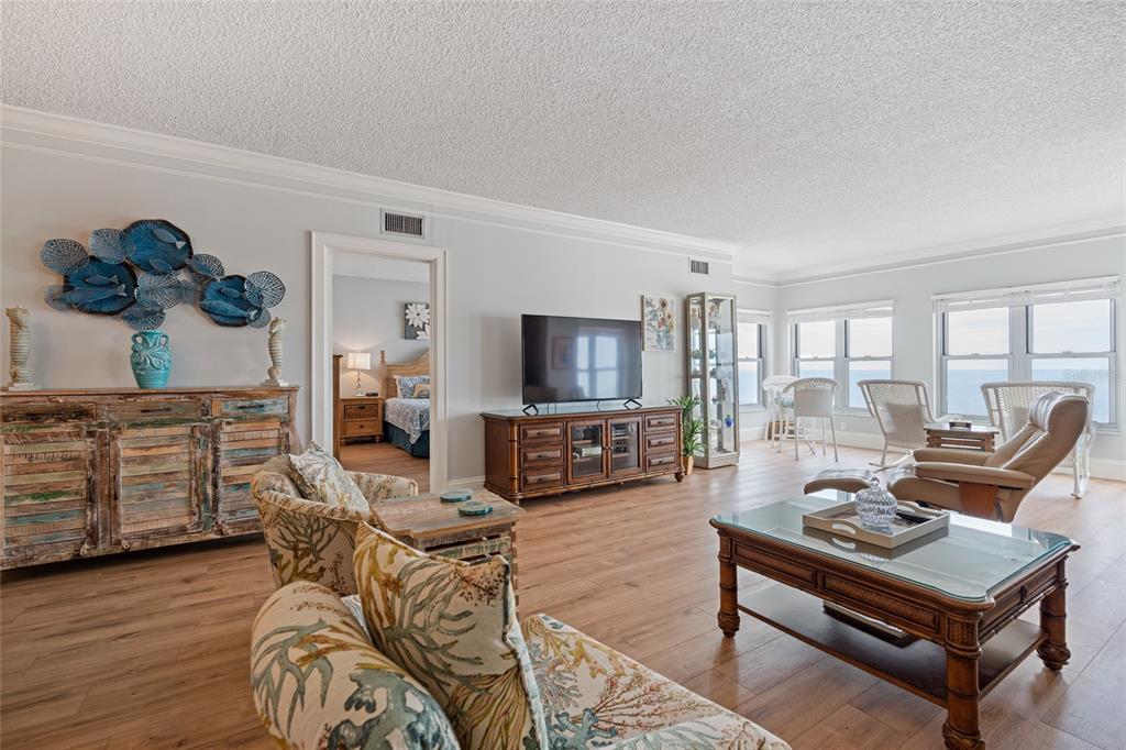 A living room features wood-look flooring, a television console, and a view of the ocean — 4950 GULF BOULEVARD UNIT 605, ST PETE BEACH, FL