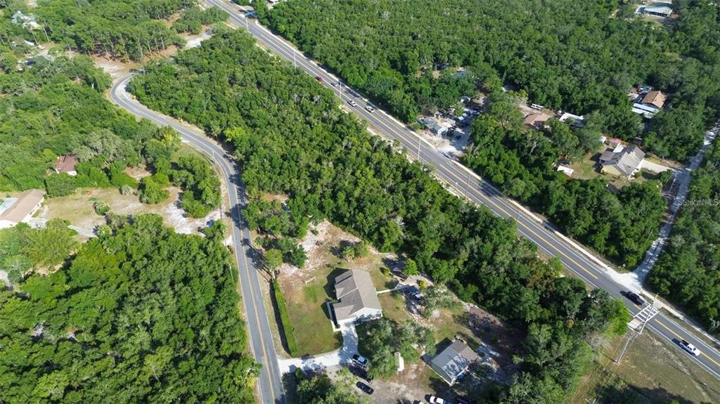 An aerial view shows a house, a smaller building, and roads surrounded by dense forest — DOYLE ROAD, DELTONA, FL