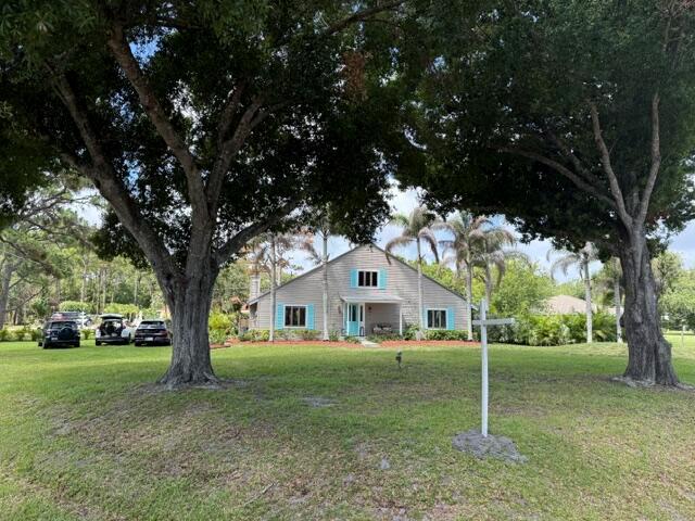 A light-colored house with blue shutters sits behind two large trees on a grassy lawn — 709 Savannah Street, Fort Pierce FL 34982, FORT PIERCE, FL