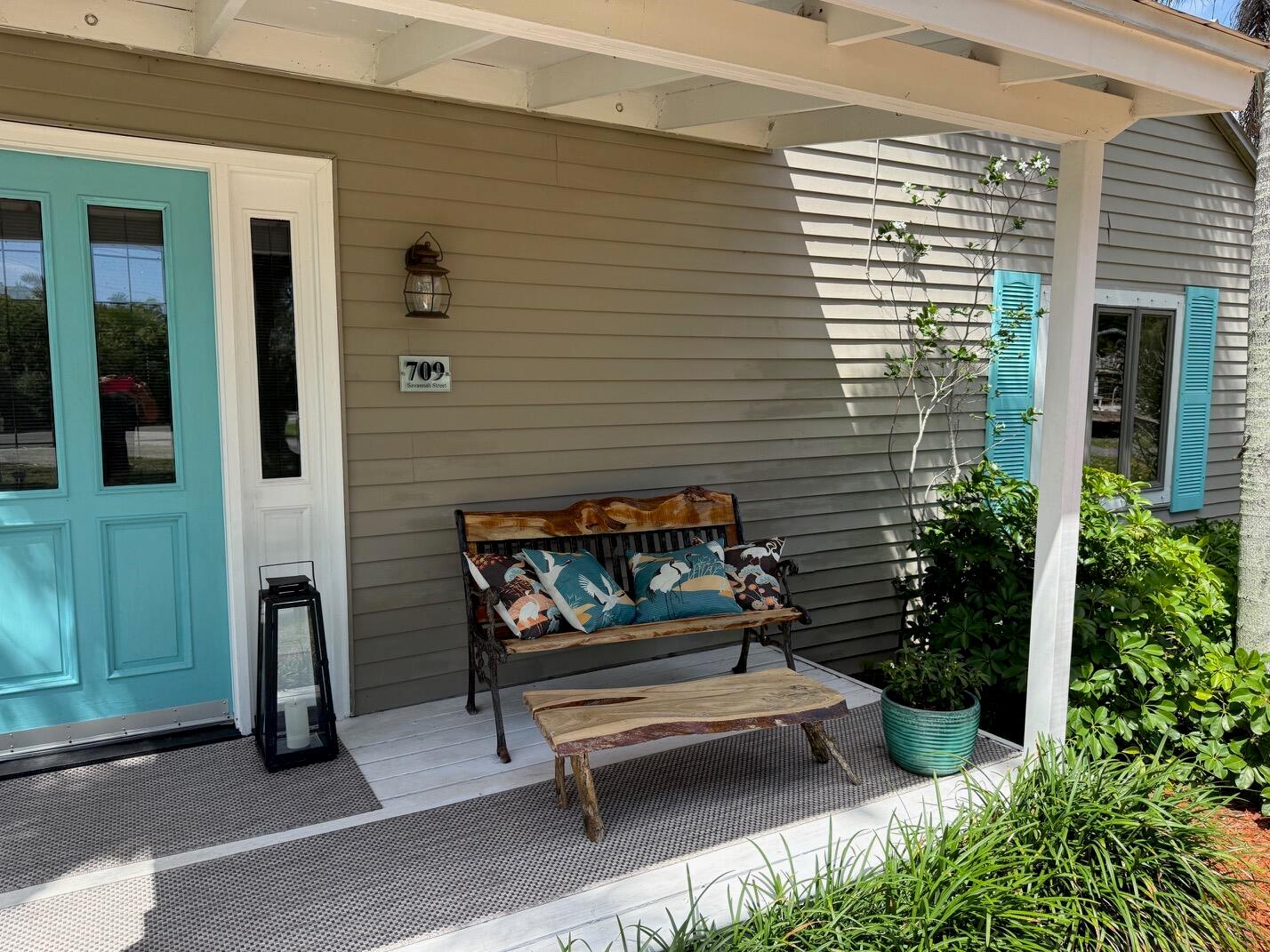 A front porch features a wooden bench with patterned pillows, a live-edge table, and a door — 709 Savannah Street, Fort Pierce FL 34982, FORT PIERCE, FL