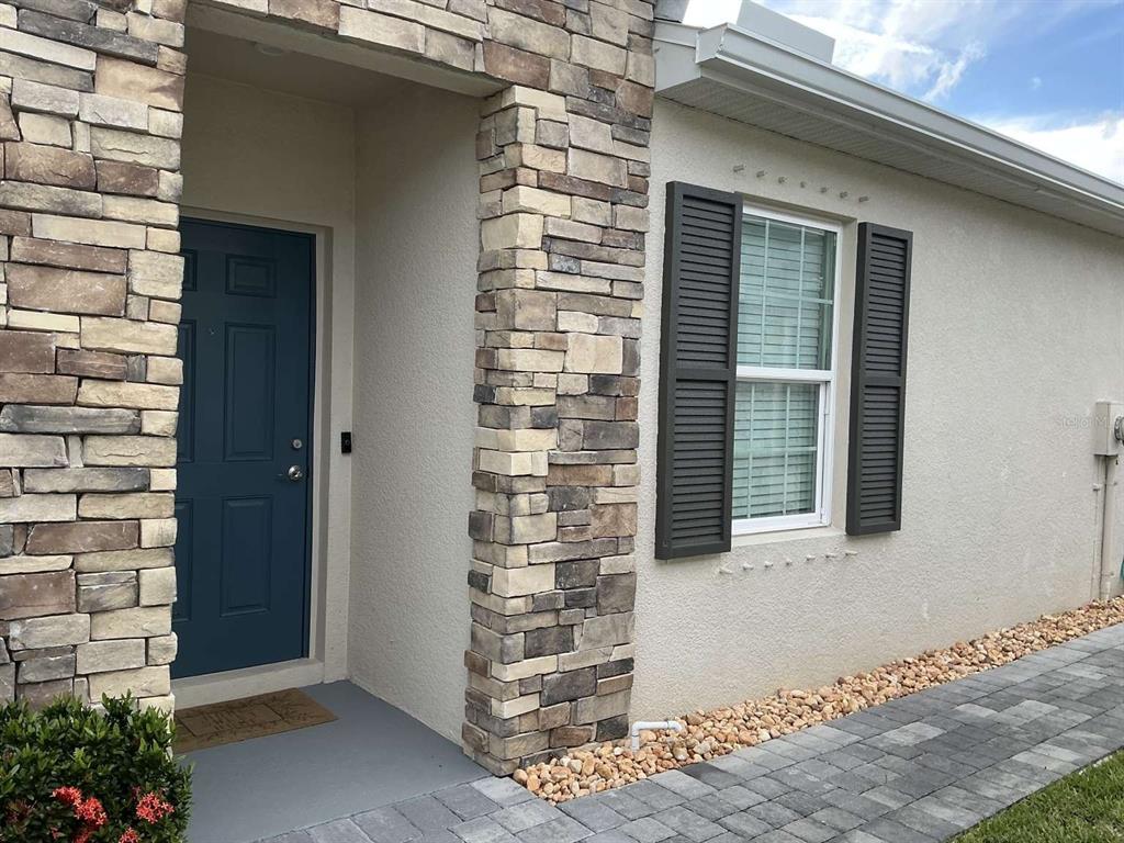 A blue front door is set into a stone-accented entryway next to a shuttered window — 1982 W PALMS DRIVE, PORT CHARLOTTE, FL