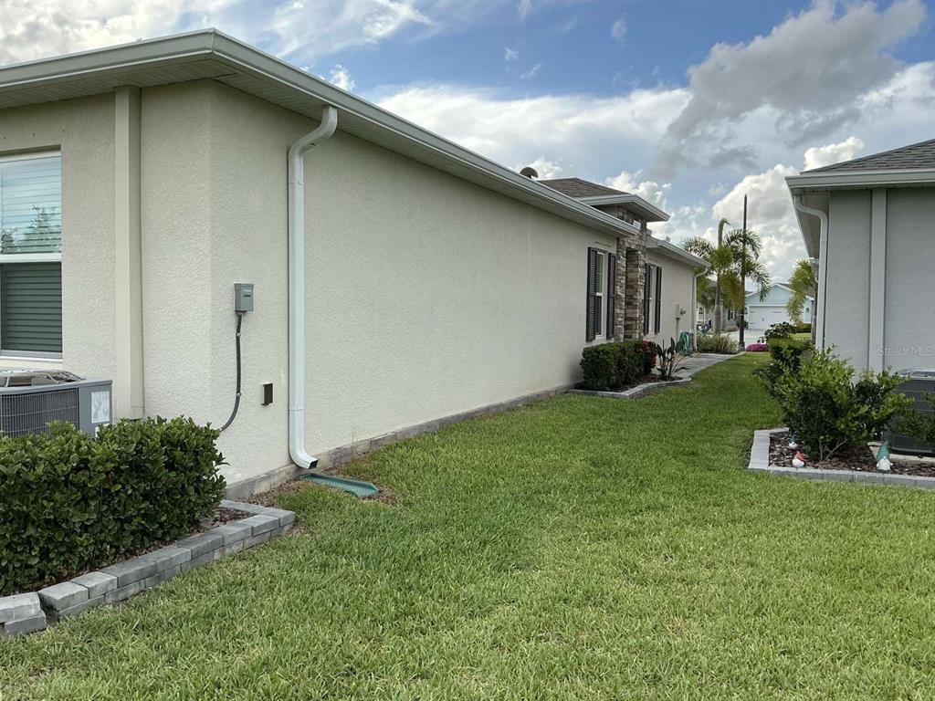 The side exterior of a beige stucco house features a downspout and a grassy yard — 1982 W PALMS DRIVE, PORT CHARLOTTE, FL