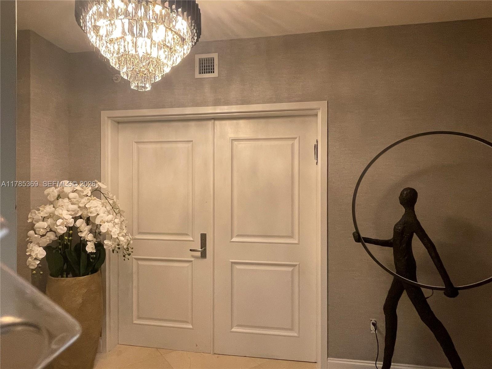 A foyer features double white doors, a crystal chandelier, a large orchid plant, and sculpture — 3101 S Ocean Dr # 1707, Hollywood FL 33019, HOLLYWOOD, FL