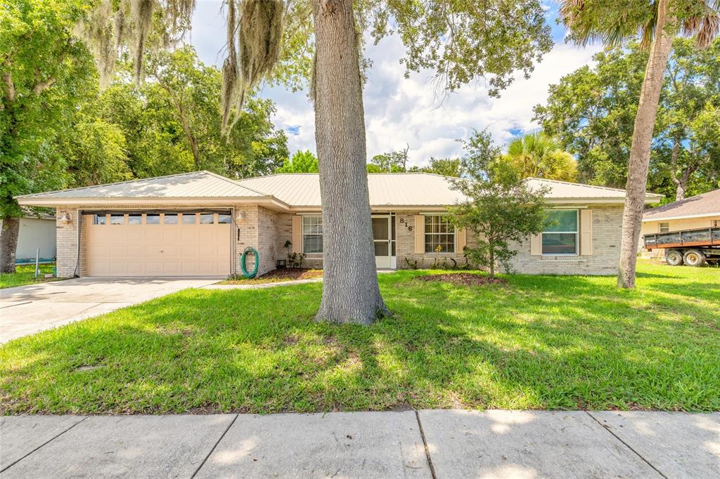 A single-story brick house with a metal roof and a large tree in the yard — 816 IRON HORSE ROAD, DAYTONA BEACH, FL