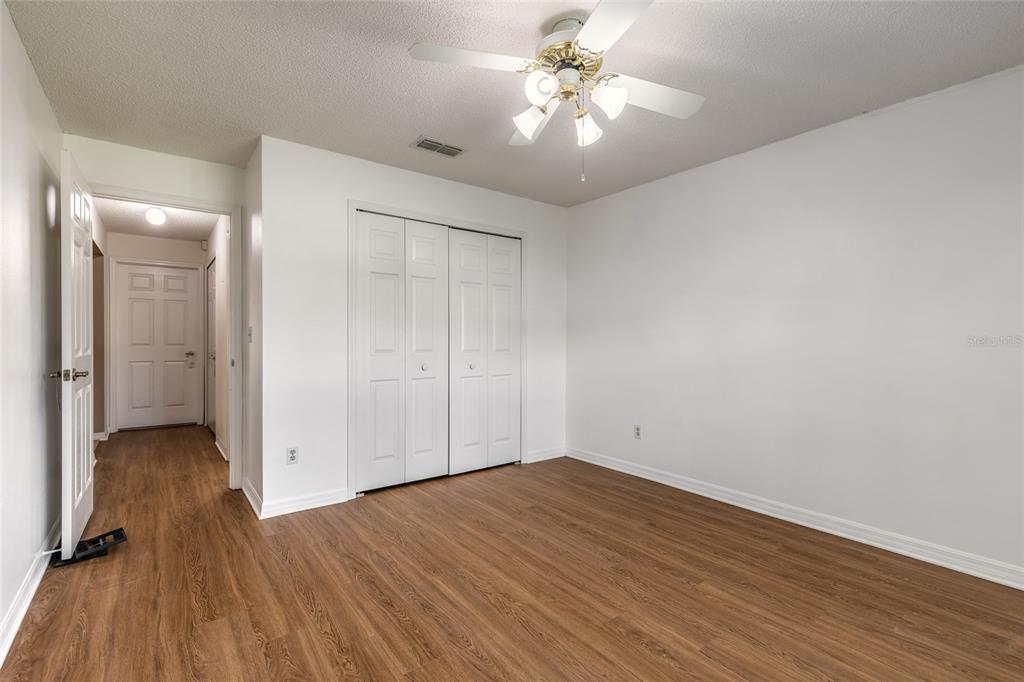 A bedroom features white walls, wood-look flooring, a ceiling fan, and a white bi-fold closet — 816 IRON HORSE ROAD, DAYTONA BEACH, FL