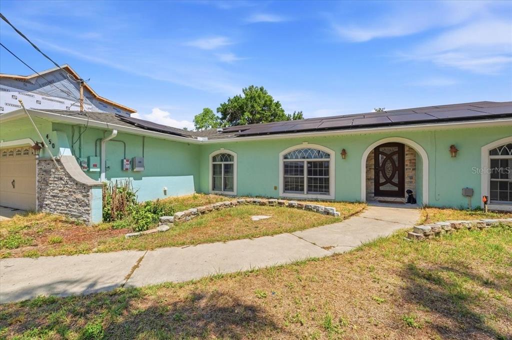 A single-story house with light green stucco walls, a stone-accented garage, and rooftop solar panels — 450 E POMELO STREET, LAKE ALFRED, FL