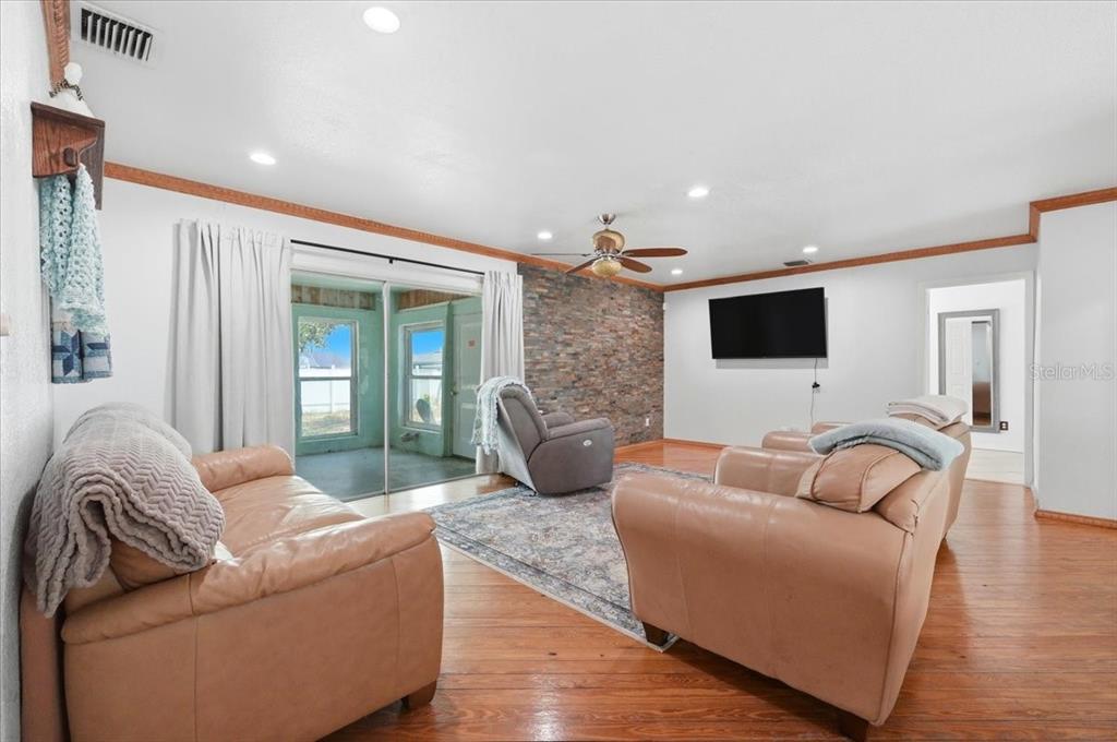 A living room features a stone accent wall, leather furniture, and hardwood floors — 450 E POMELO STREET, LAKE ALFRED, FL