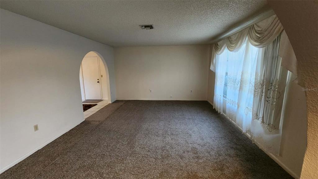 A carpeted living room features a large window with white curtains and an arched doorway — 62 SILVER LANE, OCALA, FL