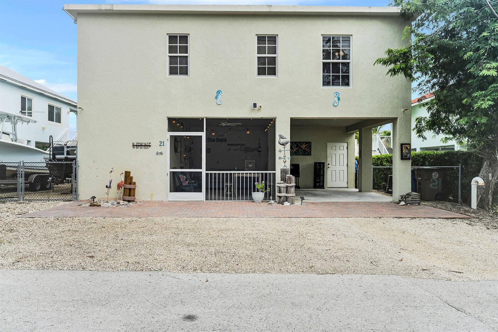 A two-story house features a screened-in patio, a covered carport, and a brick-paved driveway — 21 Poinciana Drive, Key Largo FL 33037, KEY LARGO, FL
