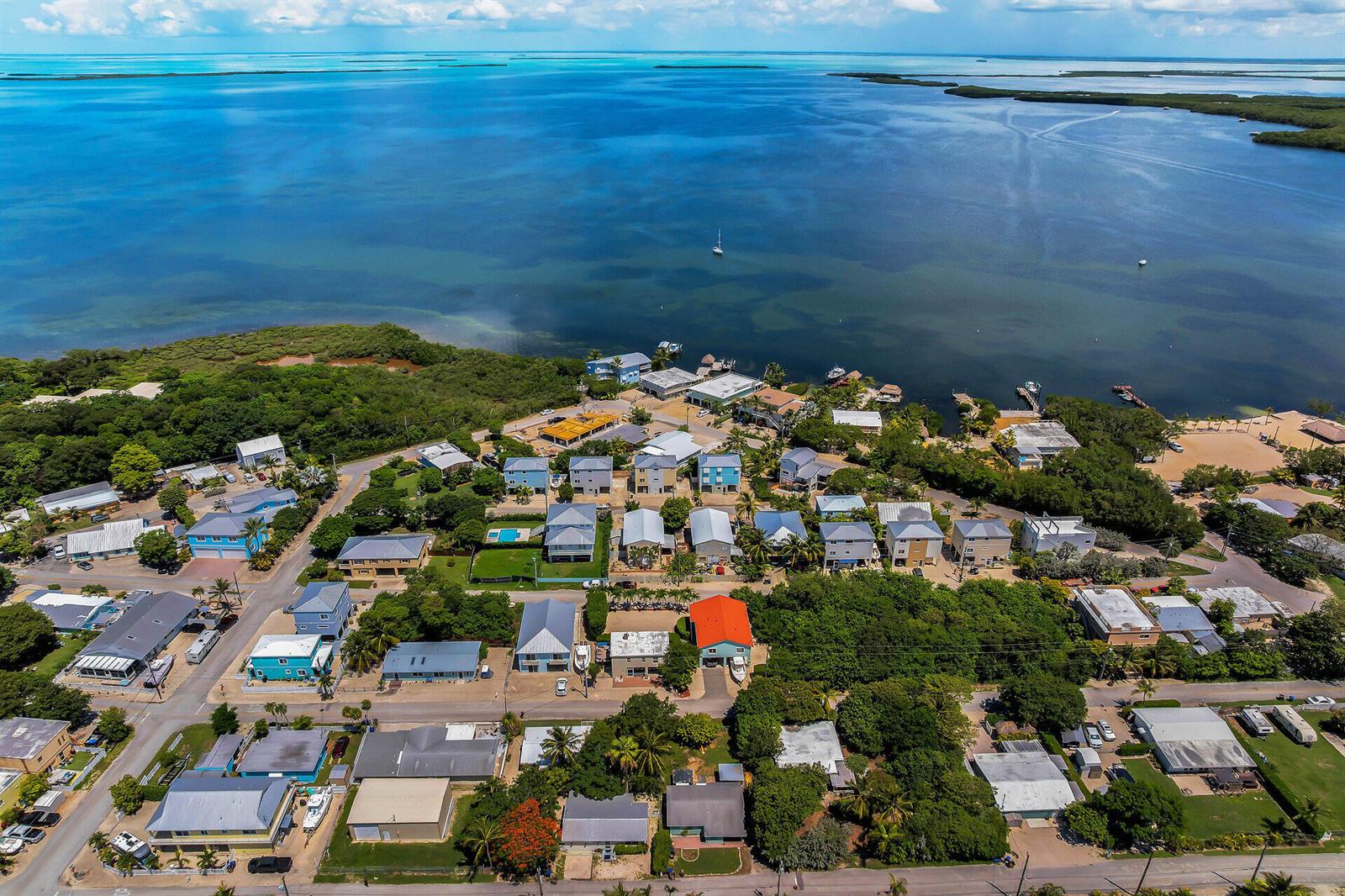 An aerial view shows a coastal neighborhood with houses nestled among trees near the water — 21 Poinciana Drive, Key Largo FL 33037, KEY LARGO, FL