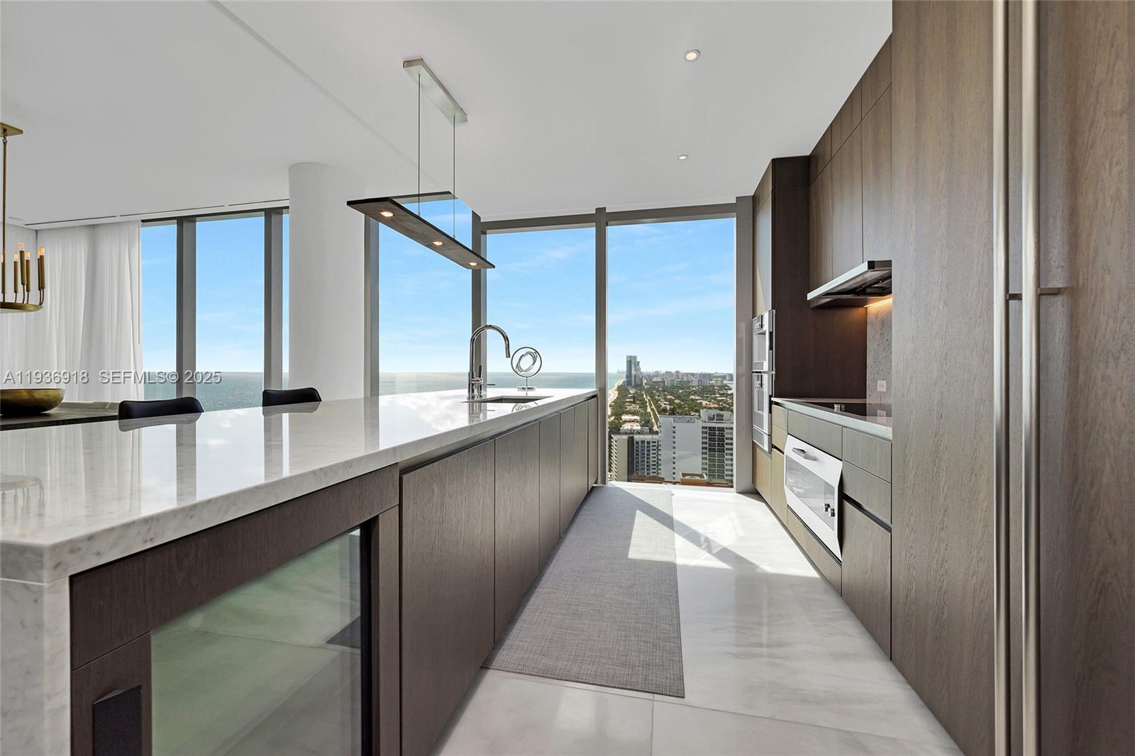 A modern kitchen features dark wood cabinetry, a marble island, and floor-to-ceiling ocean view windows — 2000 S Ocean Dr # 30B, Hallandale Beach FL 33009, HALLANDALE BEACH, FL