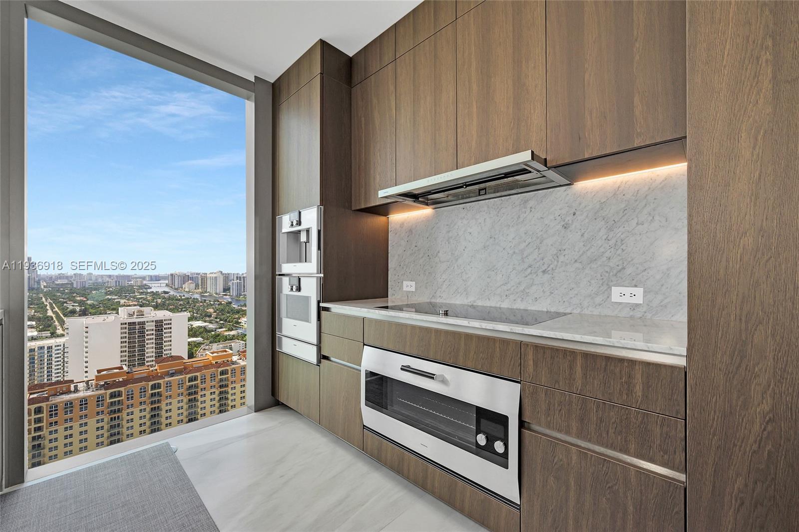 A modern kitchen features dark wood cabinetry, marble countertops, and a floor-to-ceiling window view — 2000 S Ocean Dr # 30B, Hallandale Beach FL 33009, HALLANDALE BEACH, FL