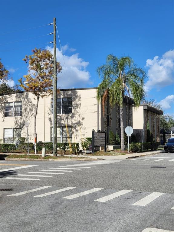 A two-story commercial building with a palm tree and a crosswalk in the foreground — 20 S ROSE AVENUE, KISSIMMEE, FL