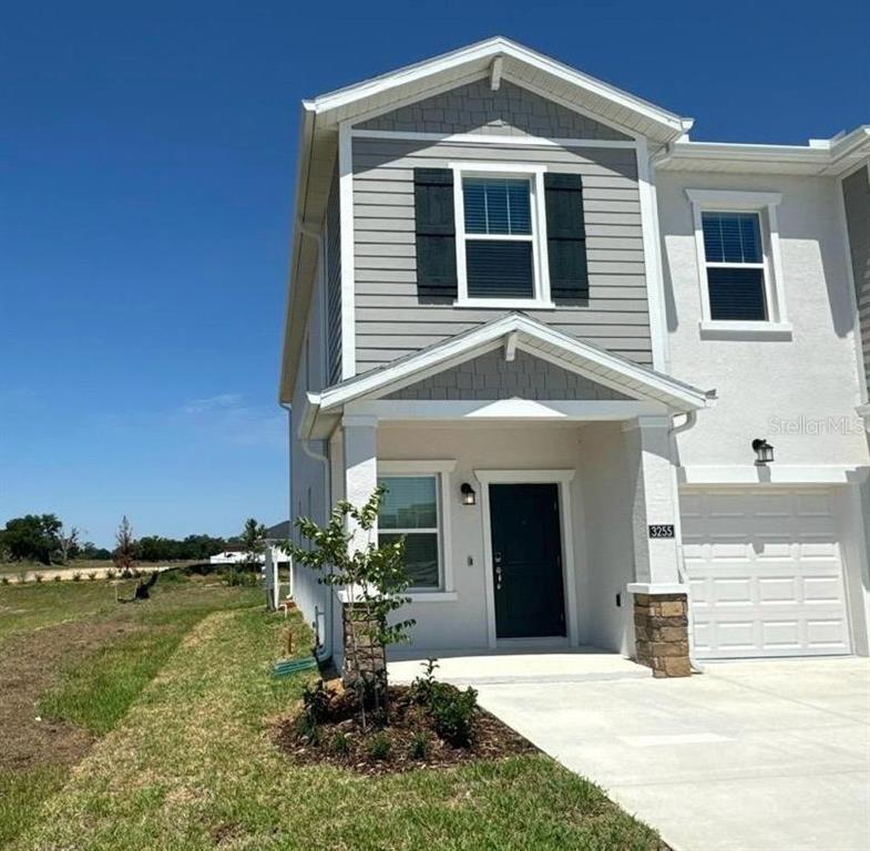A two-story townhouse with gray siding, a stone-accented pillar, and a white garage door — 3255 LAURENT LOOP, DAVENPORT, FL