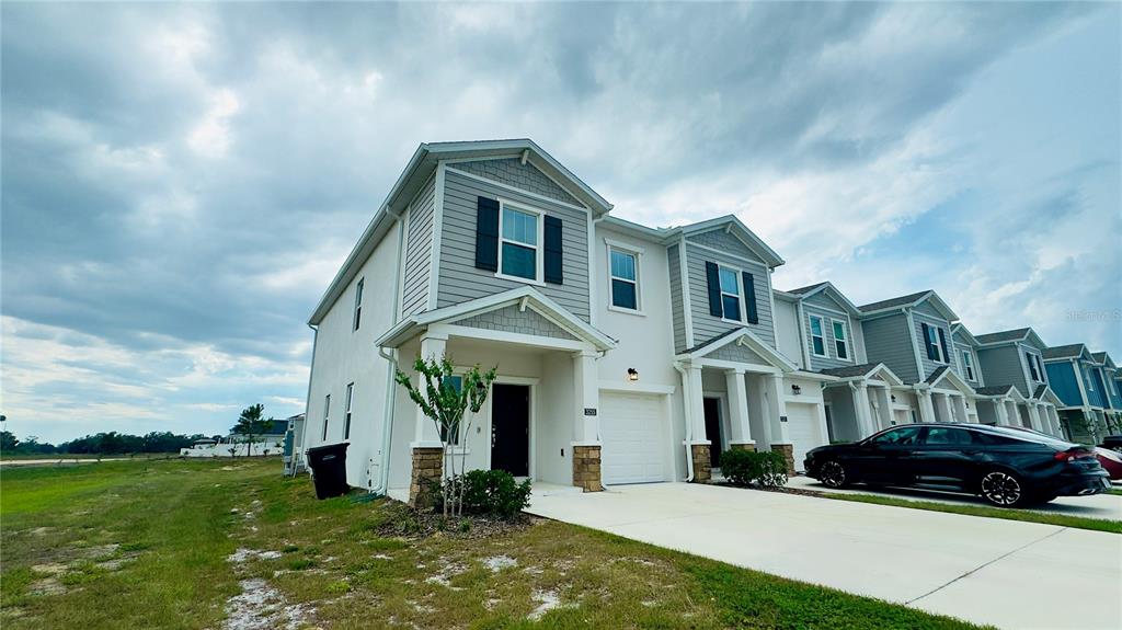 A row of two-story townhomes with light-colored siding, stone accents, and attached garages — 3255 LAURENT LOOP, DAVENPORT, FL