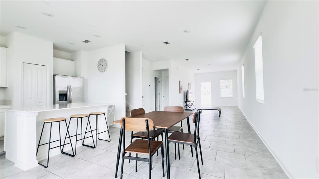 A modern open-concept kitchen and dining area features white cabinetry, stainless appliances, and tile flooring — 3255 LAURENT LOOP, DAVENPORT, FL