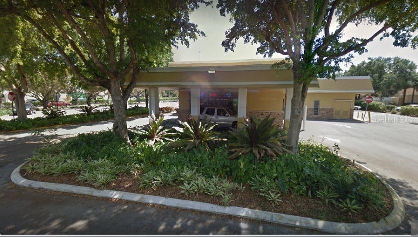A commercial building with a drive-thru lane is surrounded by mature trees and landscaped gardens — 6900 CYPRESS ROAD, PLANTATION, FL