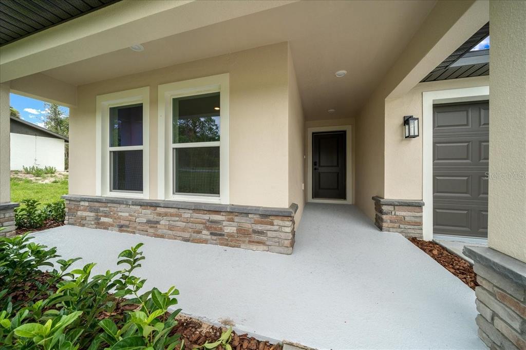 A covered front porch features a dark entry door, stone veneer accents, and two windows — 11041 SPOONBILL ROAD, WEEKI WACHEE, FL