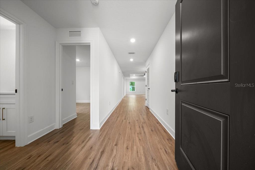 A hallway with wood-look flooring leads toward a window in a white-walled interior — 11041 SPOONBILL ROAD, WEEKI WACHEE, FL