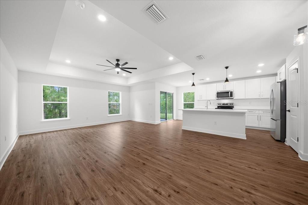 An open-concept living area features white walls, wood-look flooring, a tray ceiling, and a kitchen — 11041 SPOONBILL ROAD, WEEKI WACHEE, FL