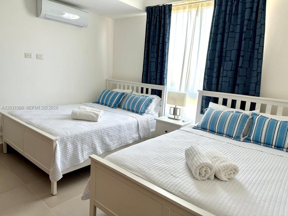 A bedroom features two white-framed beds with blue-striped pillows and dark blue curtains — 0 Punta Cana village # 0, FL, FL
