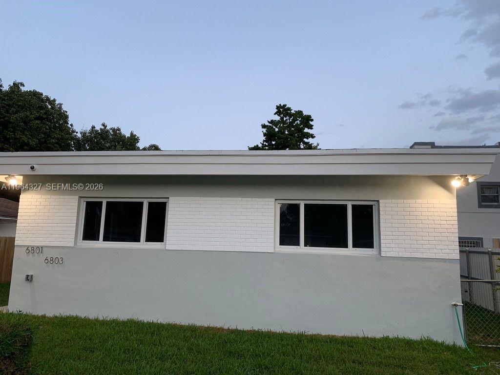 A single-story house exterior features white painted brick, a gray lower wall, and two windows — 6801 NW 2nd Ct, Miami FL 33150, MIAMI, FL