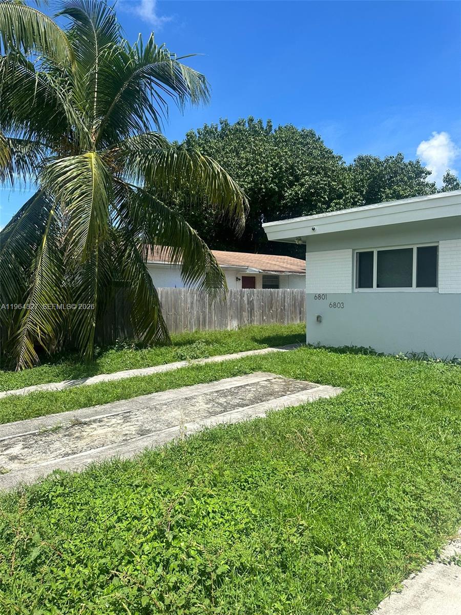 A view of a light-colored house exterior with a palm tree and overgrown grass — 6801 NW 2nd Ct, Miami FL 33150, MIAMI, FL