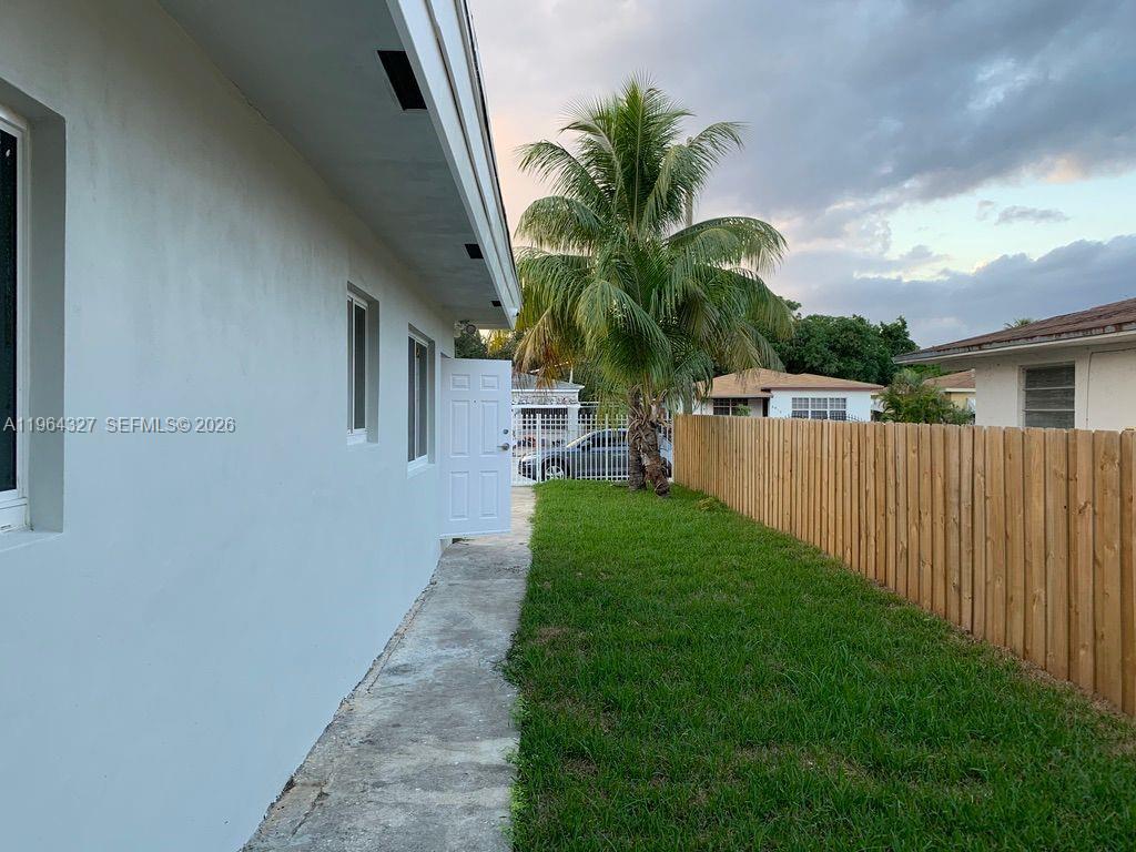 A side view of a house exterior features a white wall, a door, and a fence — 6801 NW 2nd Ct, Miami FL 33150, MIAMI, FL