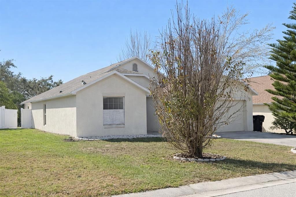A single-story house with a beige stucco exterior, a front-facing garage, and a bare tree — 551 LAKE CHARLES DRIVE, DAVENPORT, FL