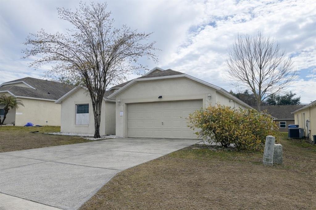 A single-story house with a beige stucco exterior, a two-car garage, and a concrete driveway — 551 LAKE CHARLES DRIVE, DAVENPORT, FL