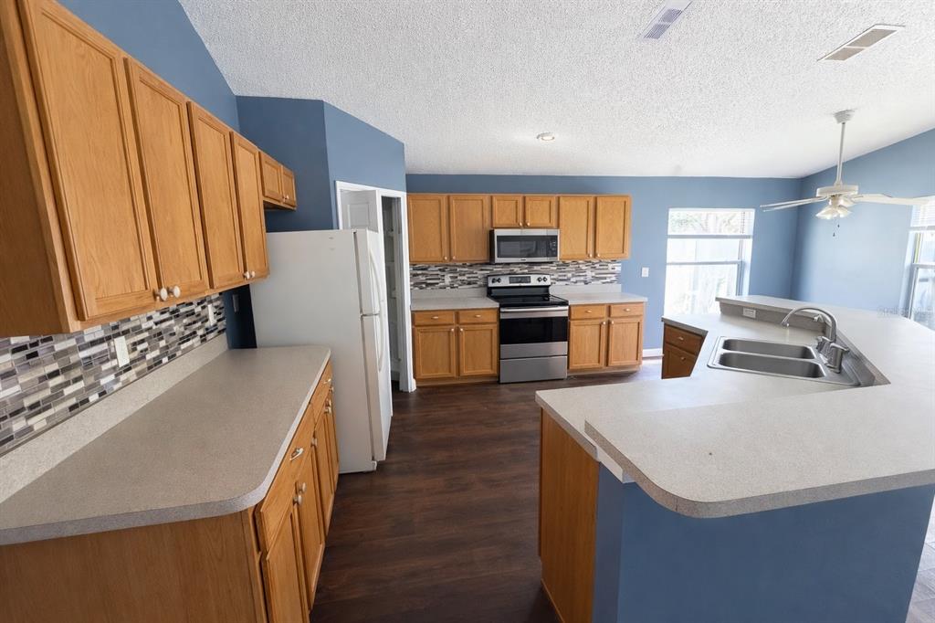 A kitchen with oak cabinets, stainless steel appliances, blue walls, and a large peninsula counter — 551 LAKE CHARLES DRIVE, DAVENPORT, FL