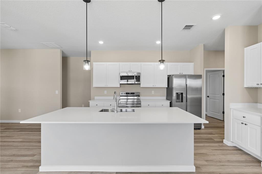 A modern kitchen features a large white island, stainless steel appliances, and white cabinetry — 4473 NW 37TH STREET ROAD, OCALA, FL
