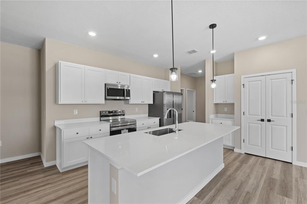 A modern kitchen features white cabinets, stainless steel appliances, a quartz island, and wood flooring — 4473 NW 37TH STREET ROAD, OCALA, FL