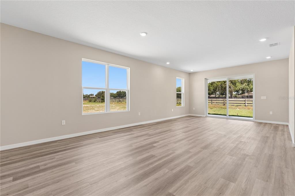 An empty living room features light-colored wood-look flooring, beige walls, and large windows and doors — 4473 NW 37TH STREET ROAD, OCALA, FL