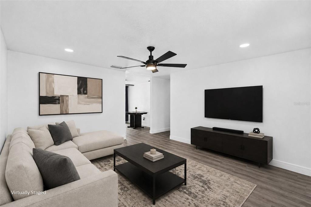 A virtually staged living room features a beige sectional, black coffee table, and wall-mounted television — 8253 GREENLEAF CIRCLE, TAMPA, FL