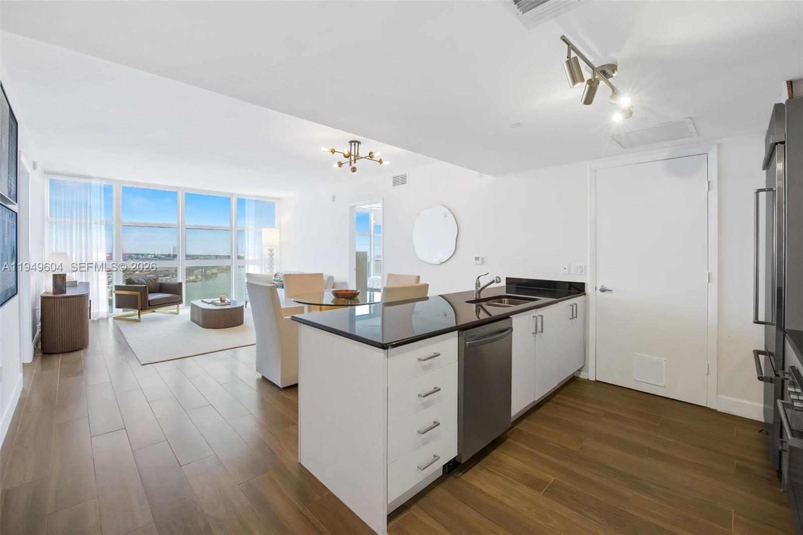 A modern kitchen with white cabinets and black countertops opens into a bright living area — 50 Biscayne Blvd # 3904, Miami FL 33132, MIAMI, FL