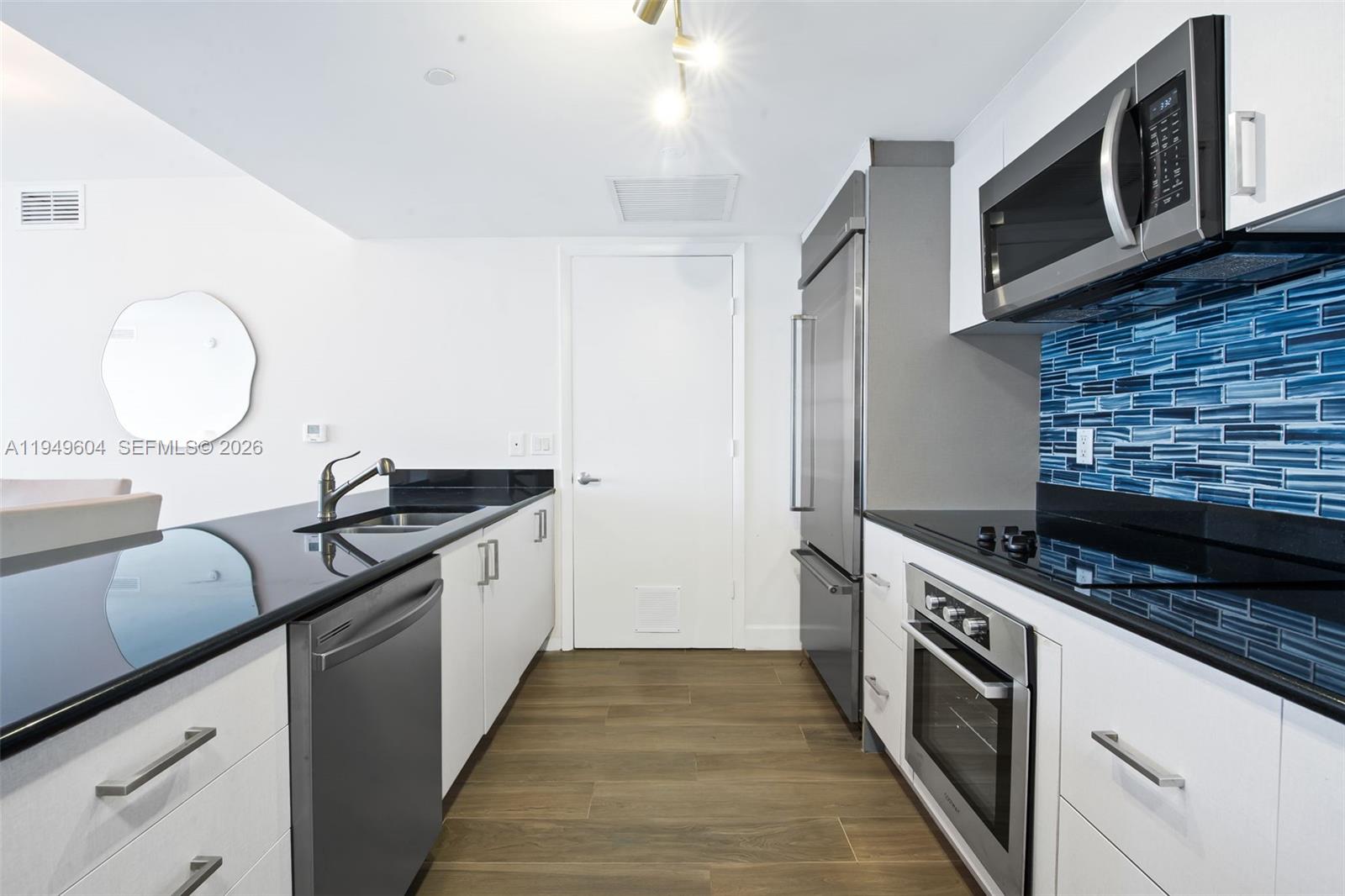 A modern kitchen features white cabinets, black countertops, stainless steel appliances, and a blue backsplash — 50 Biscayne Blvd # 3904, Miami FL 33132, MIAMI, FL