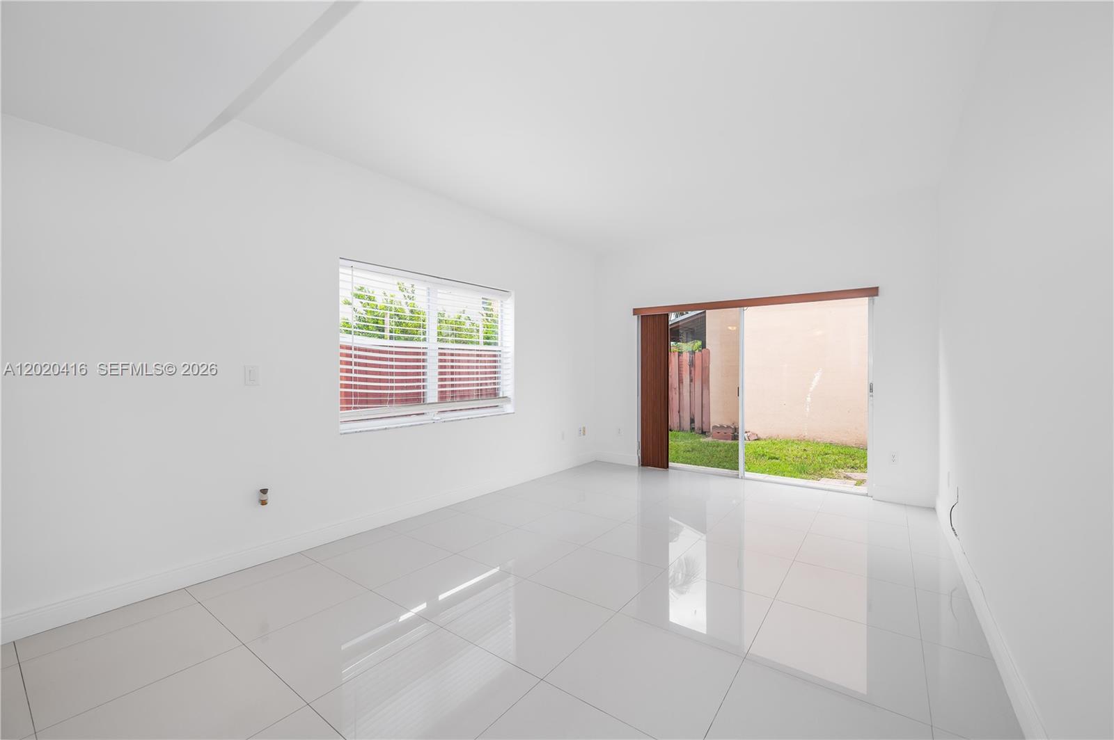 A bright, empty room features white walls, glossy tile flooring, a window, and sliding doors — 4668 SW 153rd Ct, Miami FL 33185, MIAMI, FL
