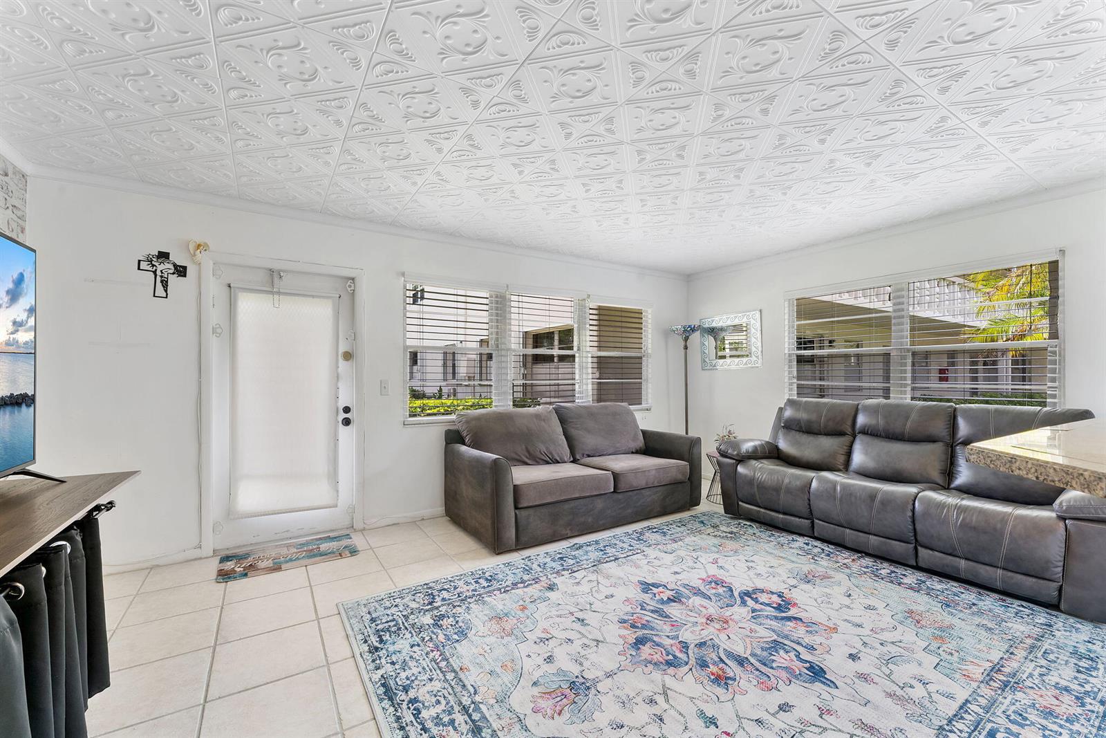 A living room features a patterned tin ceiling, tile floors, and two gray sofas — 269 S Ventnor S # 269, Deerfield Beach FL 33442, DEERFIELD BEACH, FL