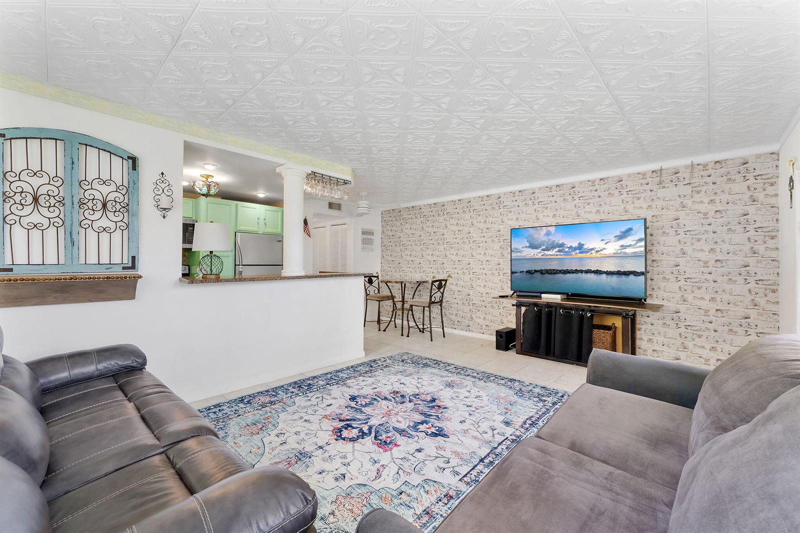 A living room features a patterned ceiling, brick-look wallpaper, and an open kitchen pass-through — 269 S Ventnor S # 269, Deerfield Beach FL 33442, DEERFIELD BEACH, FL
